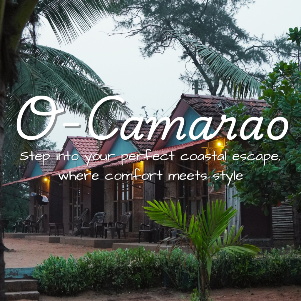 O Camarão Goa guesthouse exterior showing traditional Portuguese-style architecture with red tile roofs, wooden balconies, and tropical landscaping including coconut palms and lush greenery, featuring the tagline 'Step into your perfect coastal escape, where comfort meets style'