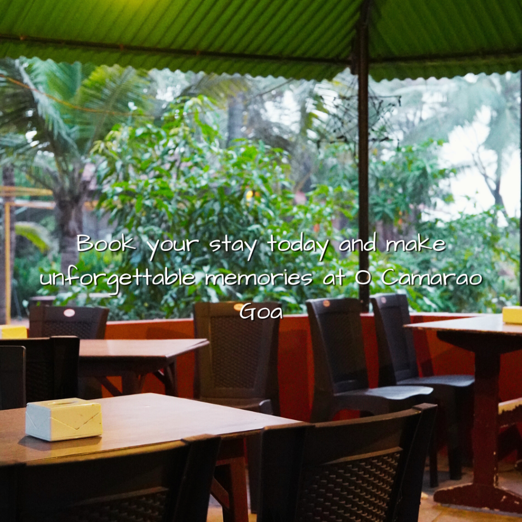 O Camarão Goa outdoor dining area with wooden tables and chairs set up for al fresco meals, surrounded by lush tropical greenery and palm trees, featuring the promotional text 'Book your stay today and make unforgettable memories at O Camarão Goa