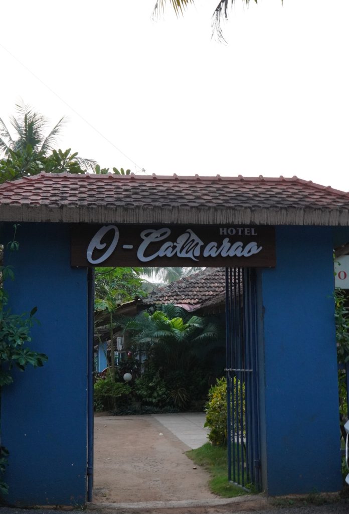 Blue-painted archway entrance of O-Camarao Guest House flanked by tropical greenery on Calangute Beach, Goa